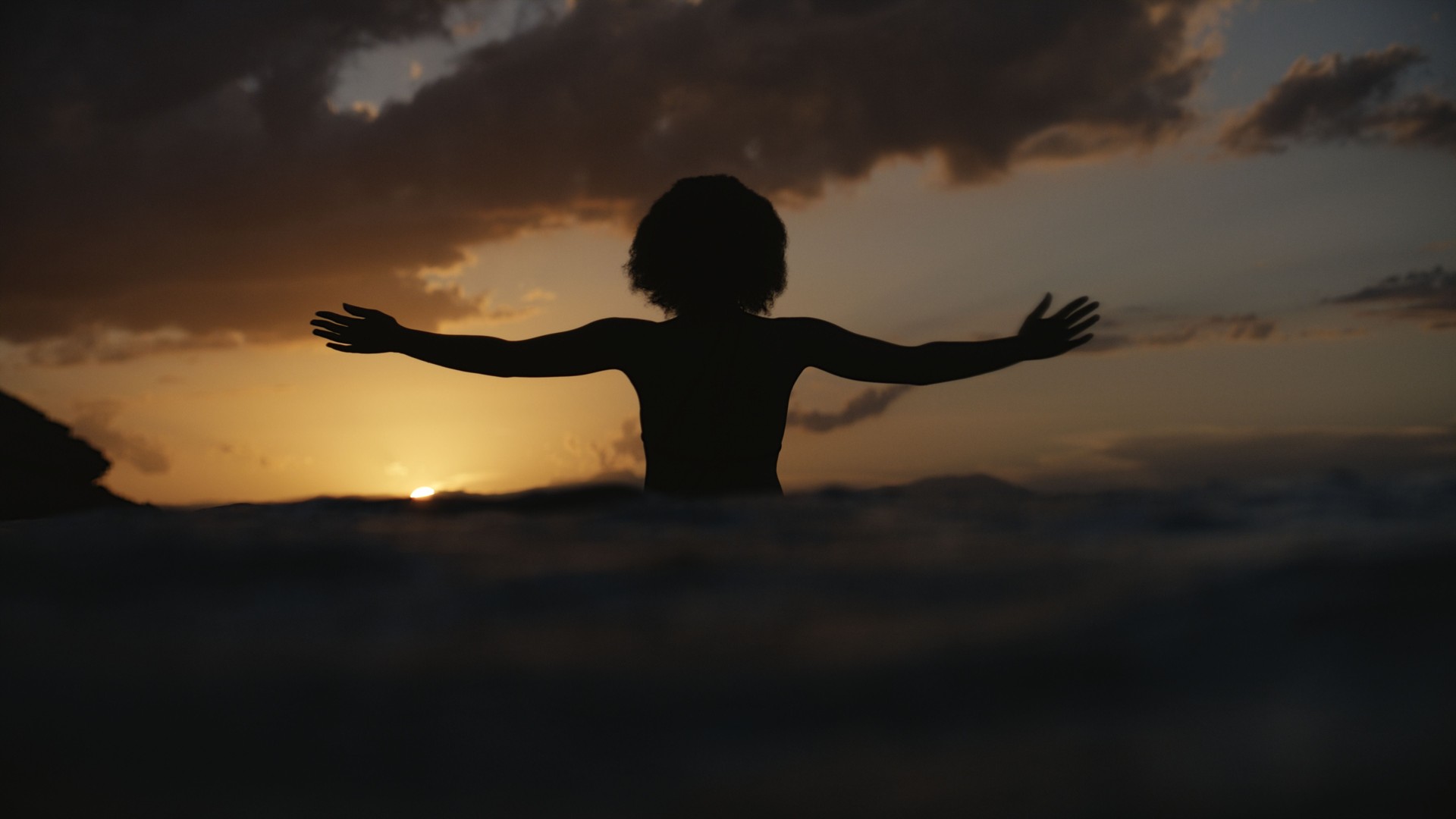 African ethnicity woman in the sea at sunset. Meditating and praying to the sun. One with nature