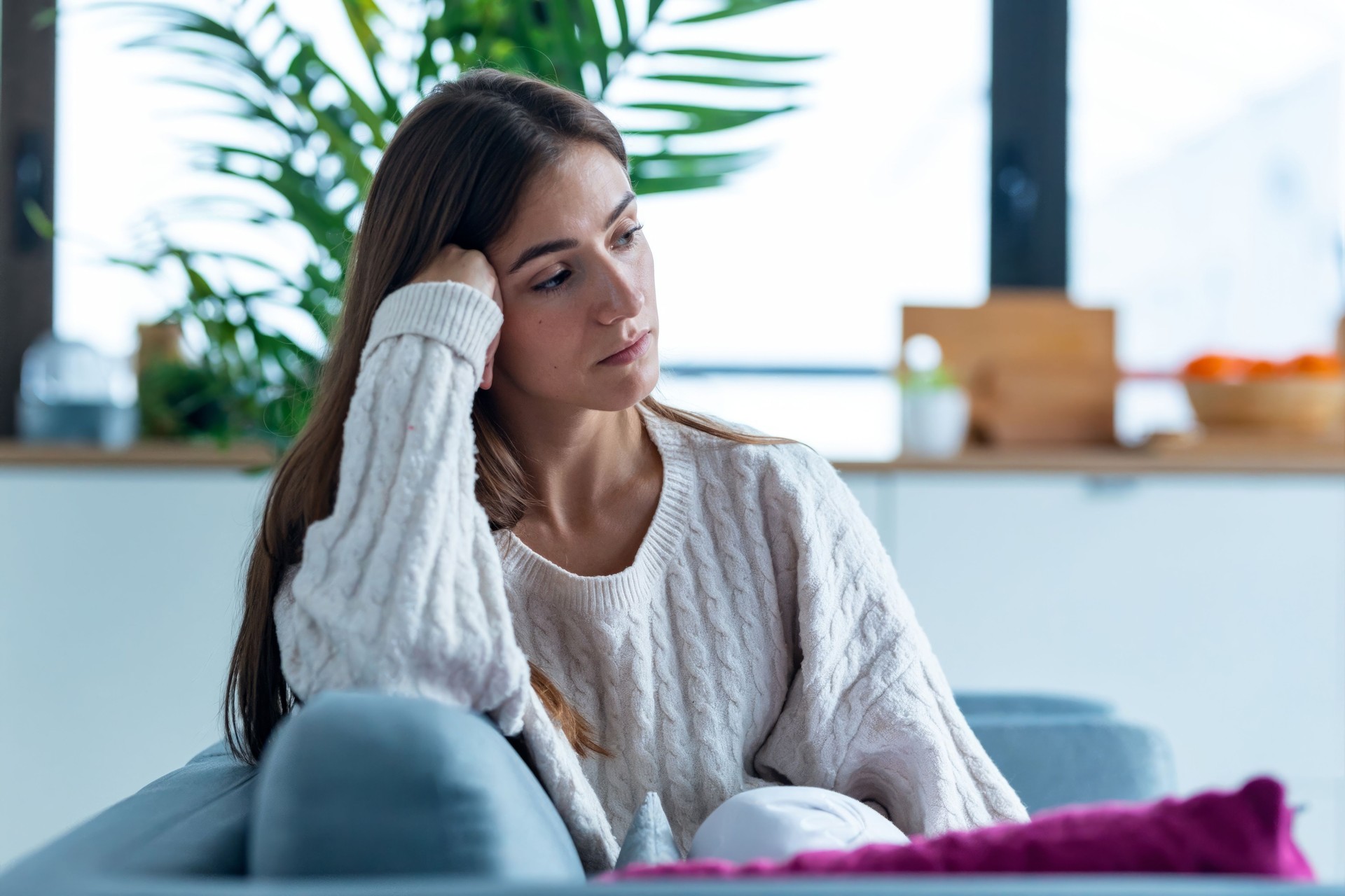 Depressed young woman thinking about her problems while sitting on the sofa at home.